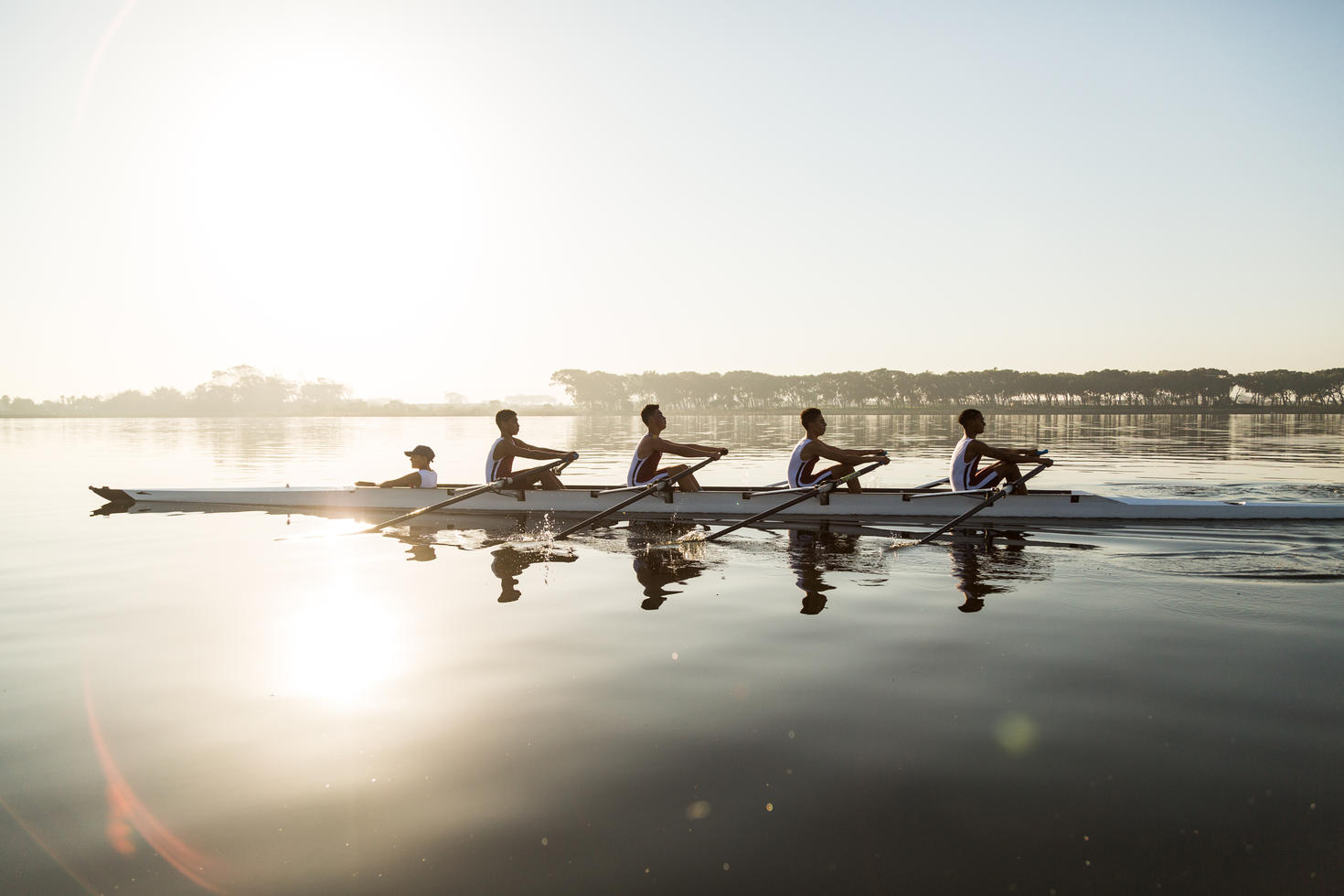 5 people rowing on the water at sunset
