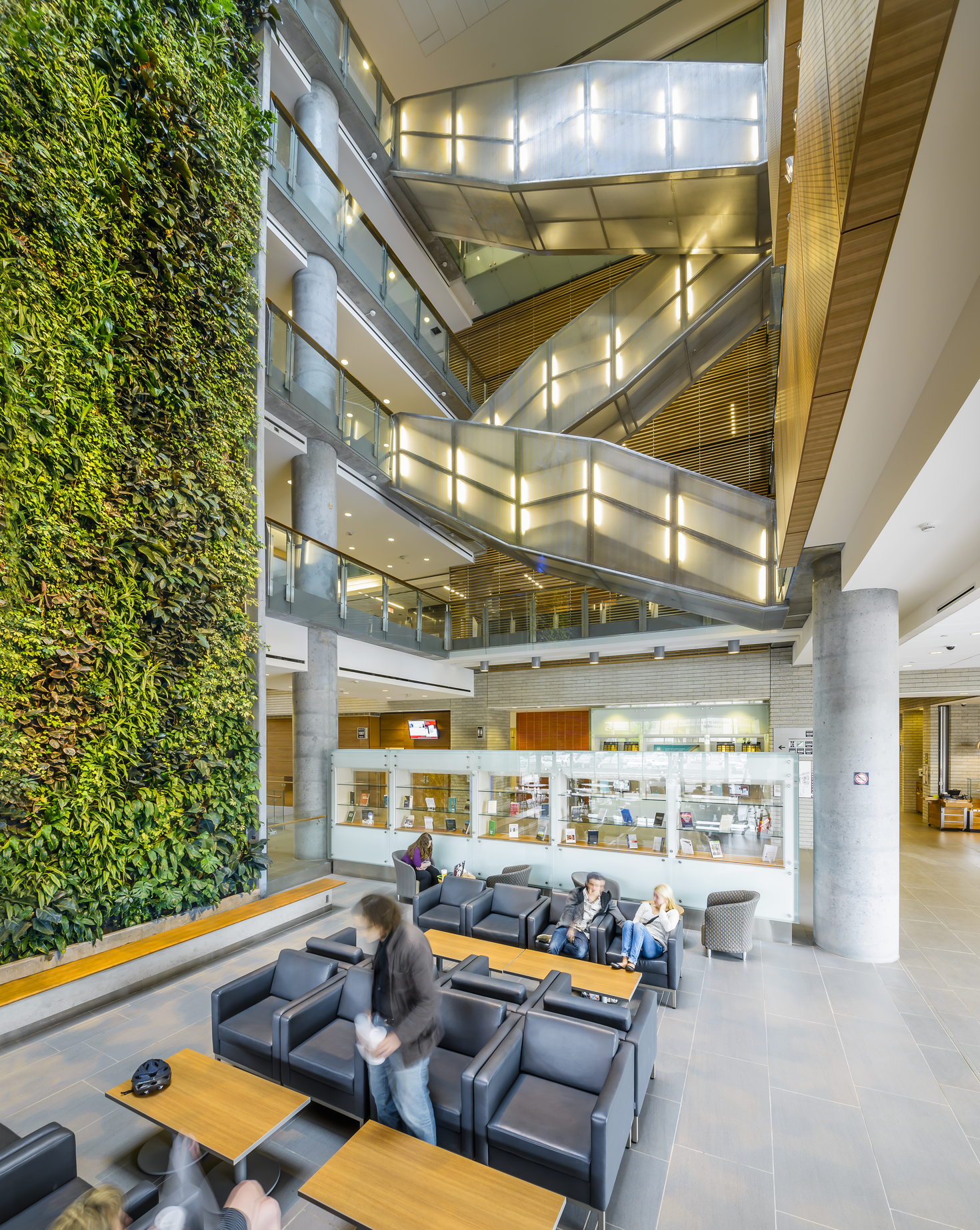 Inside campus building, with modern staircase in center and green plant wall to the left. 