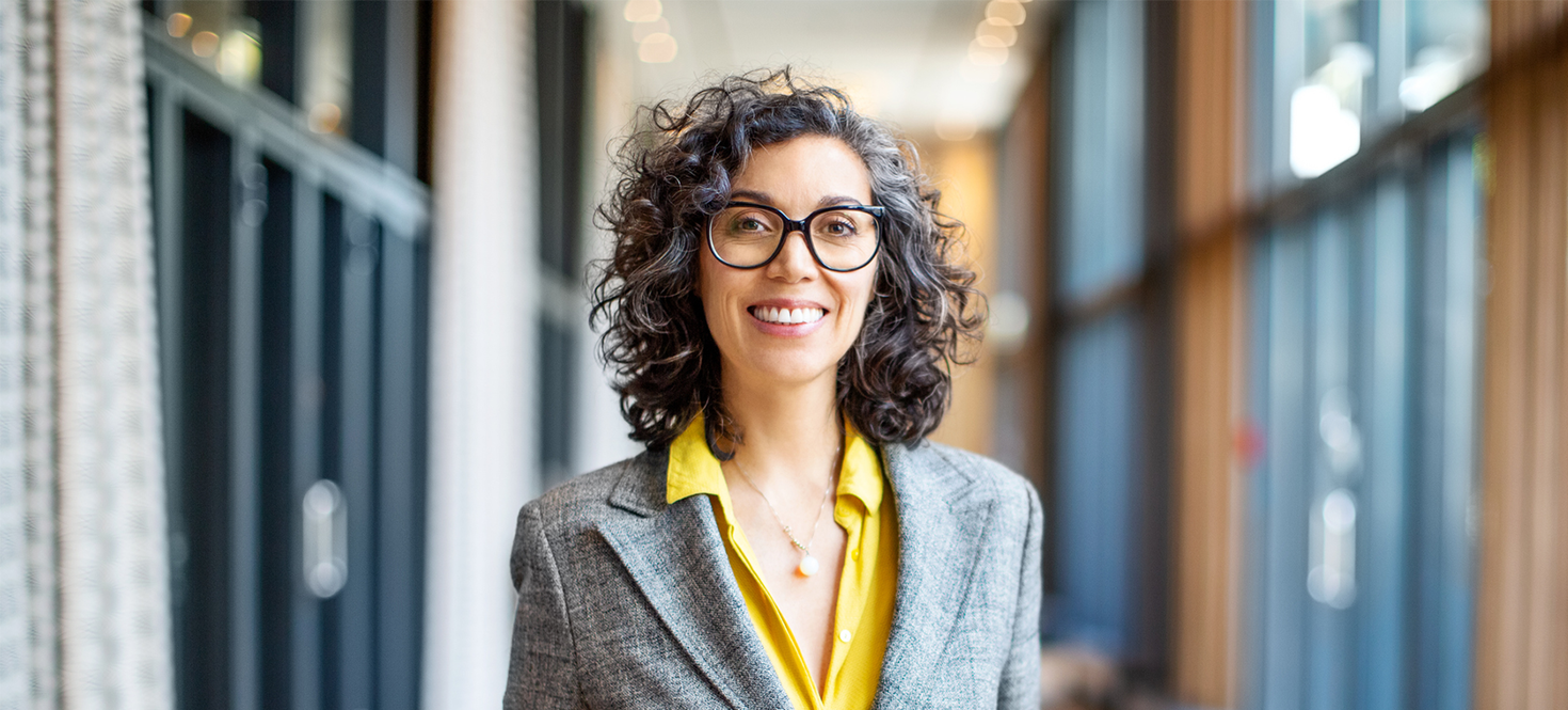 Senior executive standing with hands in pockets in hallway.