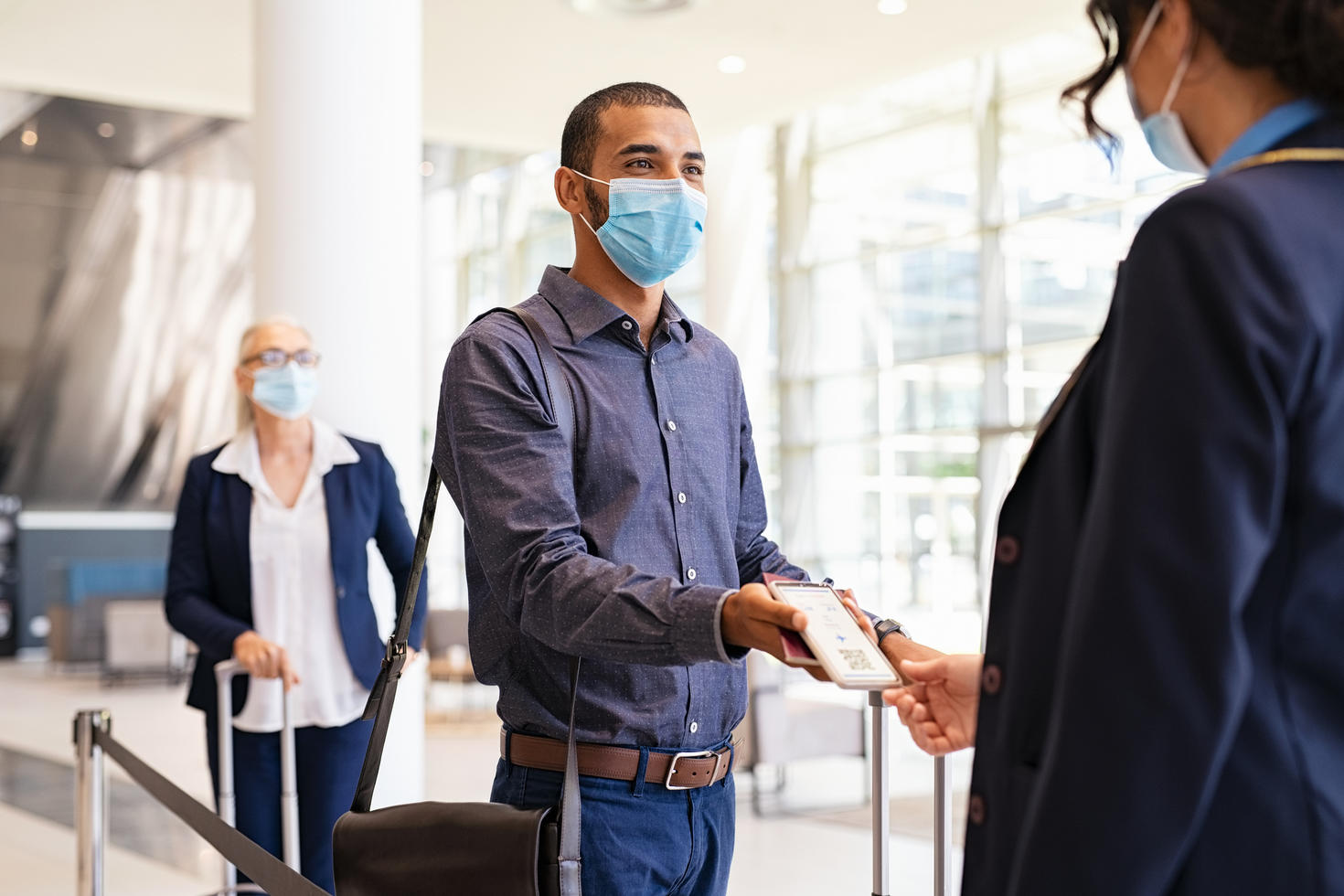 Person in airport with mask showing boarding ticket.