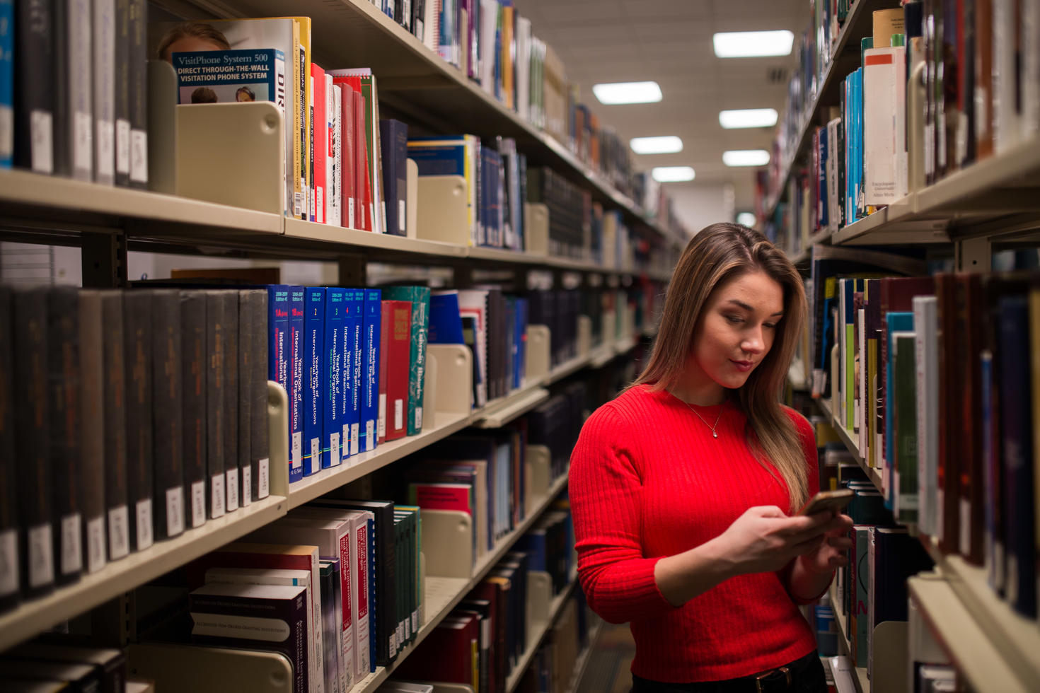 Girl stands in a library, between two rows of books