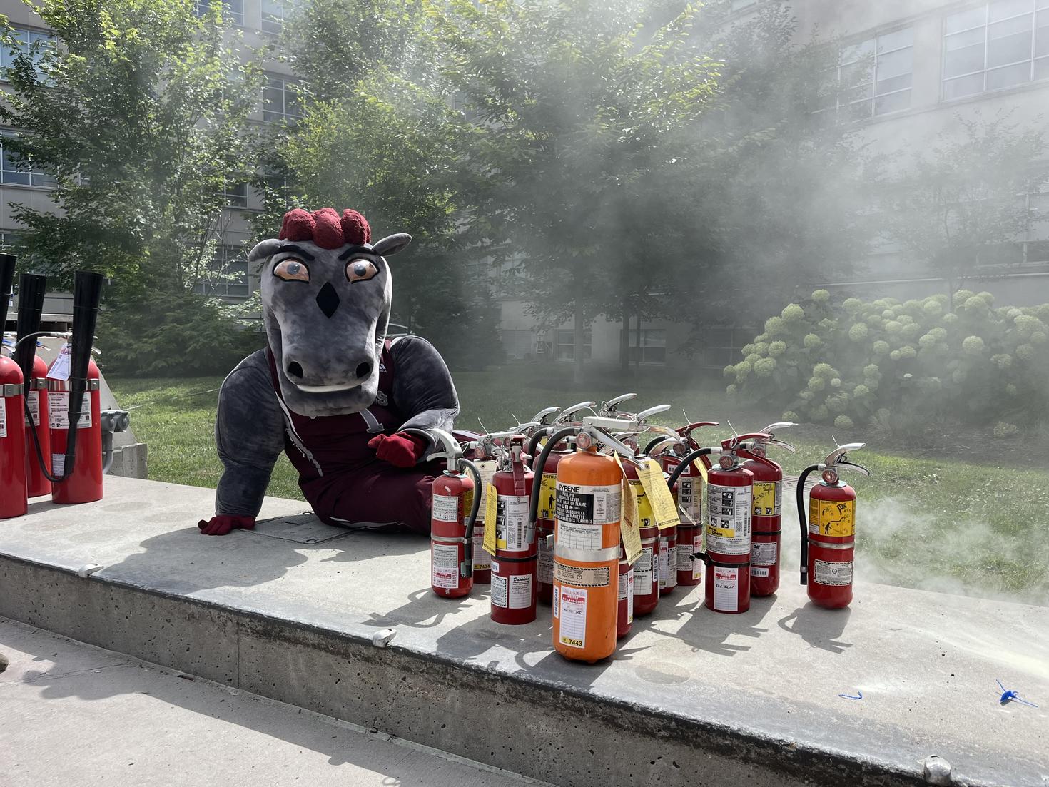 Gee-gees mascot posing beside fire extinguishers. 