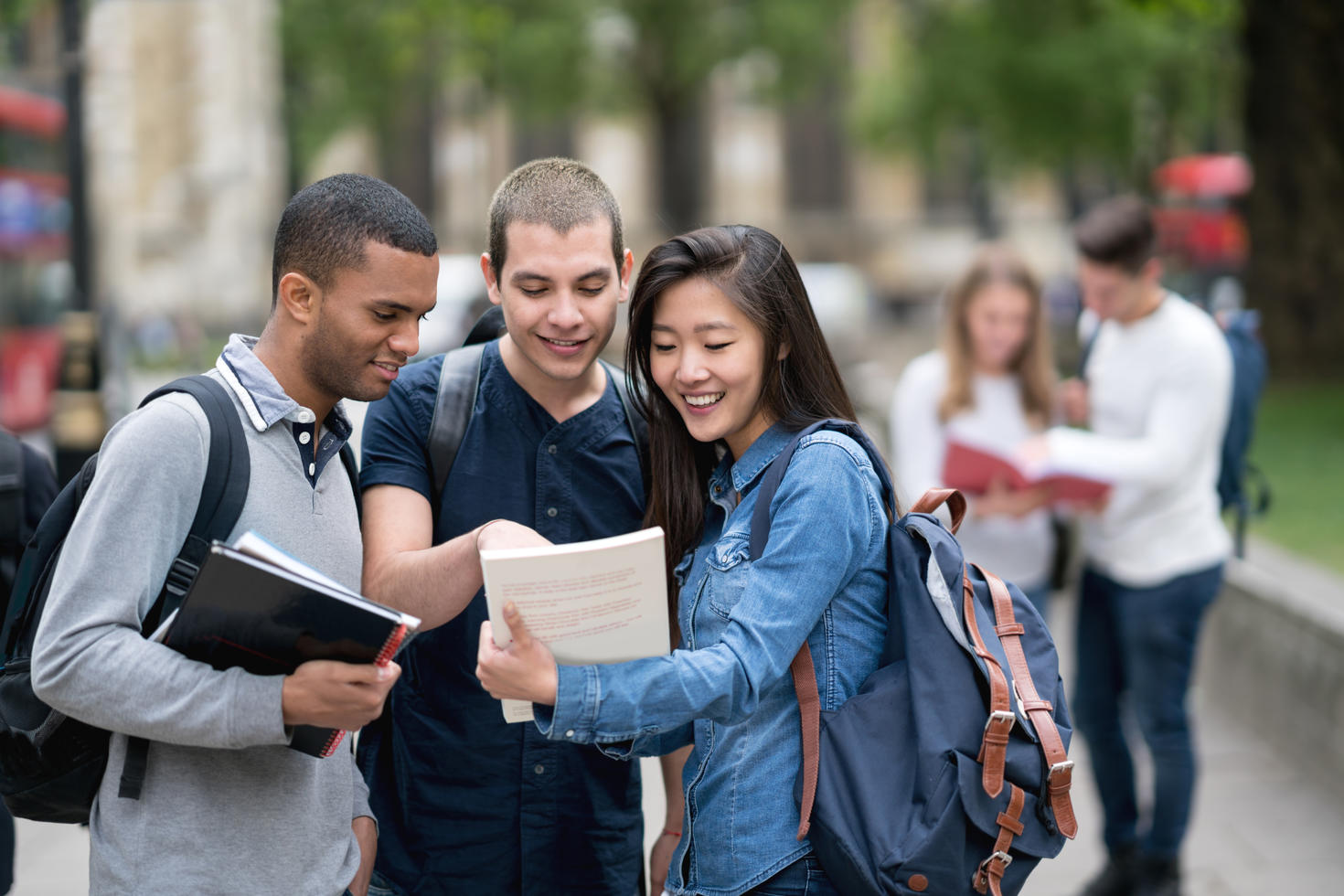Three student standing outside and looking at a book