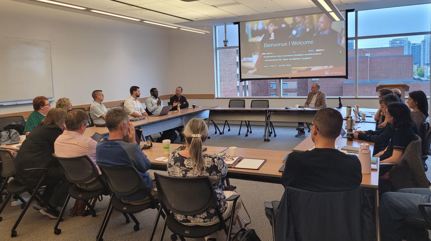 professors in a uOttawa conference room, listening to a speaker holding a microphone