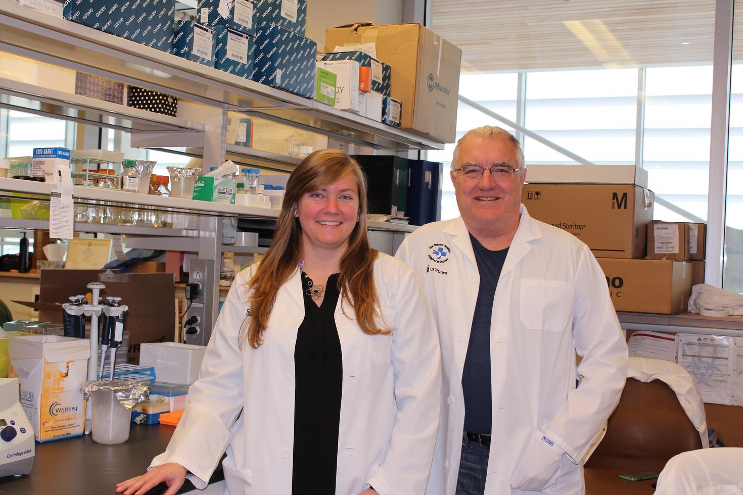 A woman and man stand, in white coats, in a research laboratory.