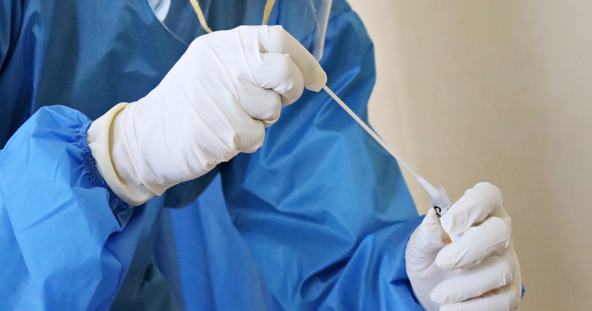 Someone wearing PPE and holding a cotton swab