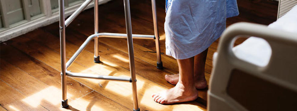 Man wearing a hospital gown shown using a walker