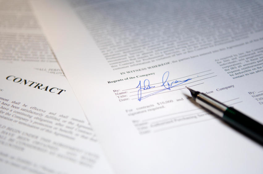 Contrats papier étalés sur le bureau avec un stylo.