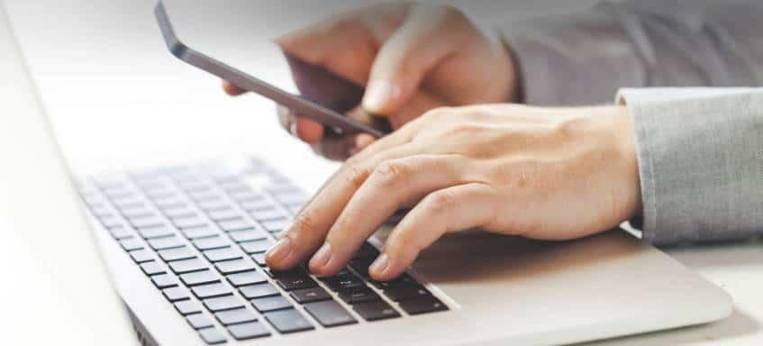 Une main sur l'ordinateur portable et l'autre sur le téléphone portable