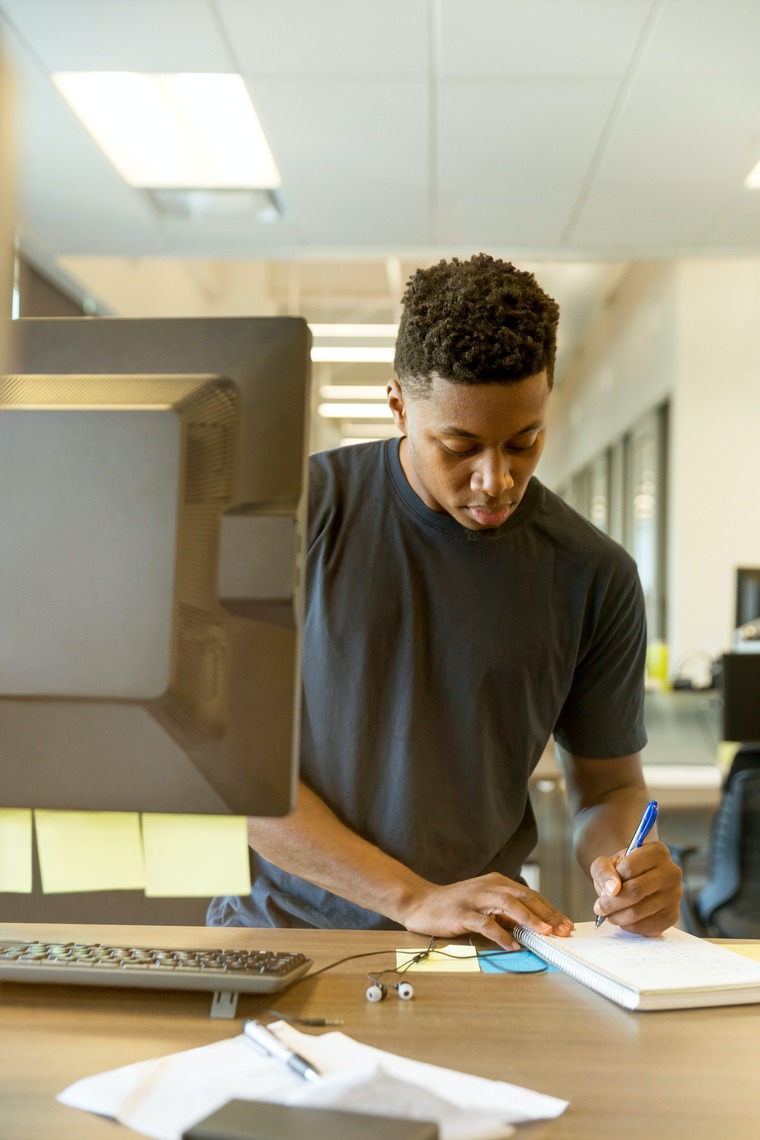 man taking notes next to a computer 