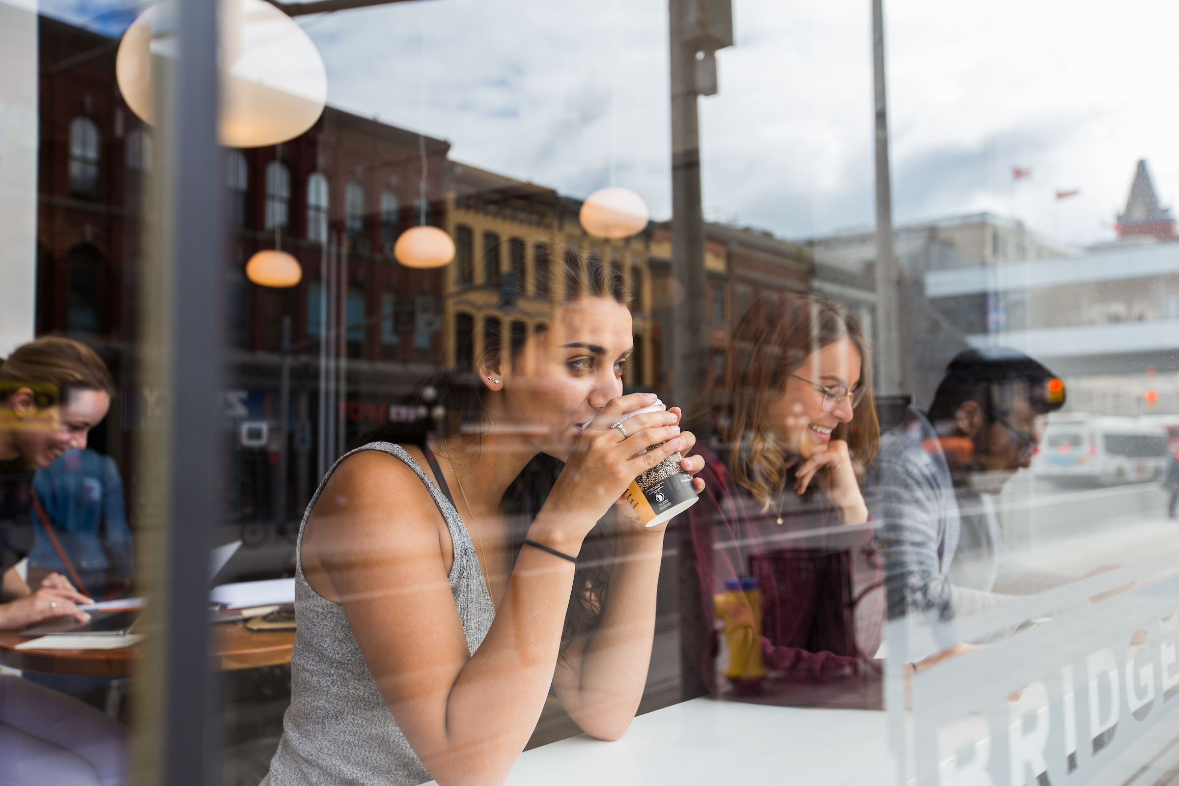 Woman seen through a window at a coffee shop drinking from a cup 