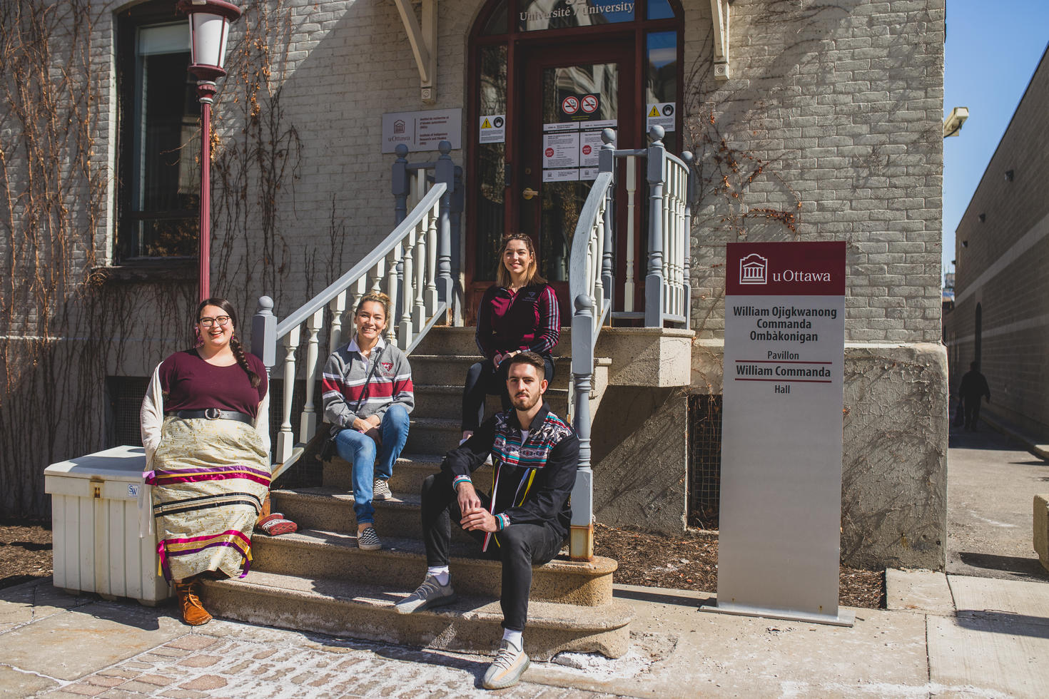 Four Indigenous students sit on the steps of a building on campus. A uOttawa sign is visible.