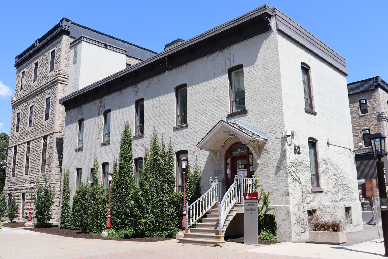 : Image shows the Institute of Indigenous Research and Studies on the University of Ottawa campus. It is a white brick building with one side partially covered in vines.