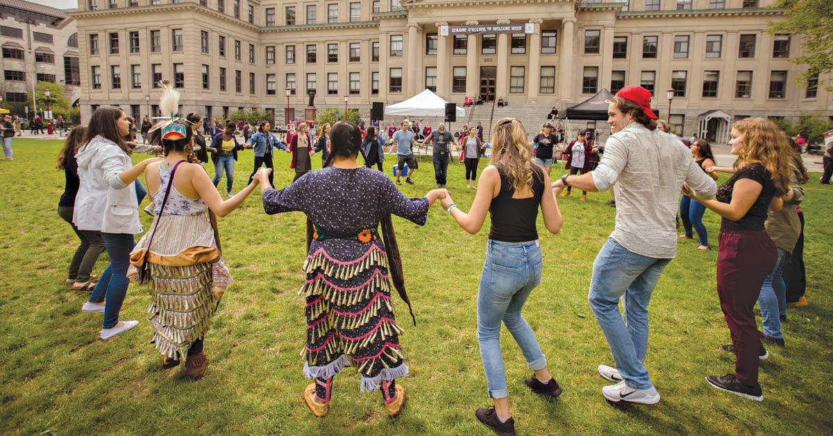 Students on Tabaret Lawn holding hands and dancing in circle. 