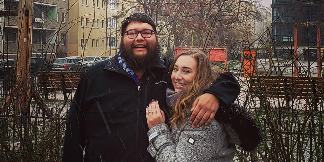 A man and woman pose together with a residentail area in the background.