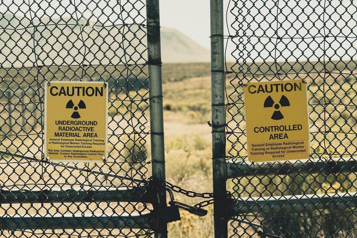 Pair of nuclear radiation signs hang on chain link fence in dessert