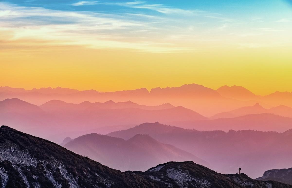 Hiker atop mountain looking off into multicolored distance