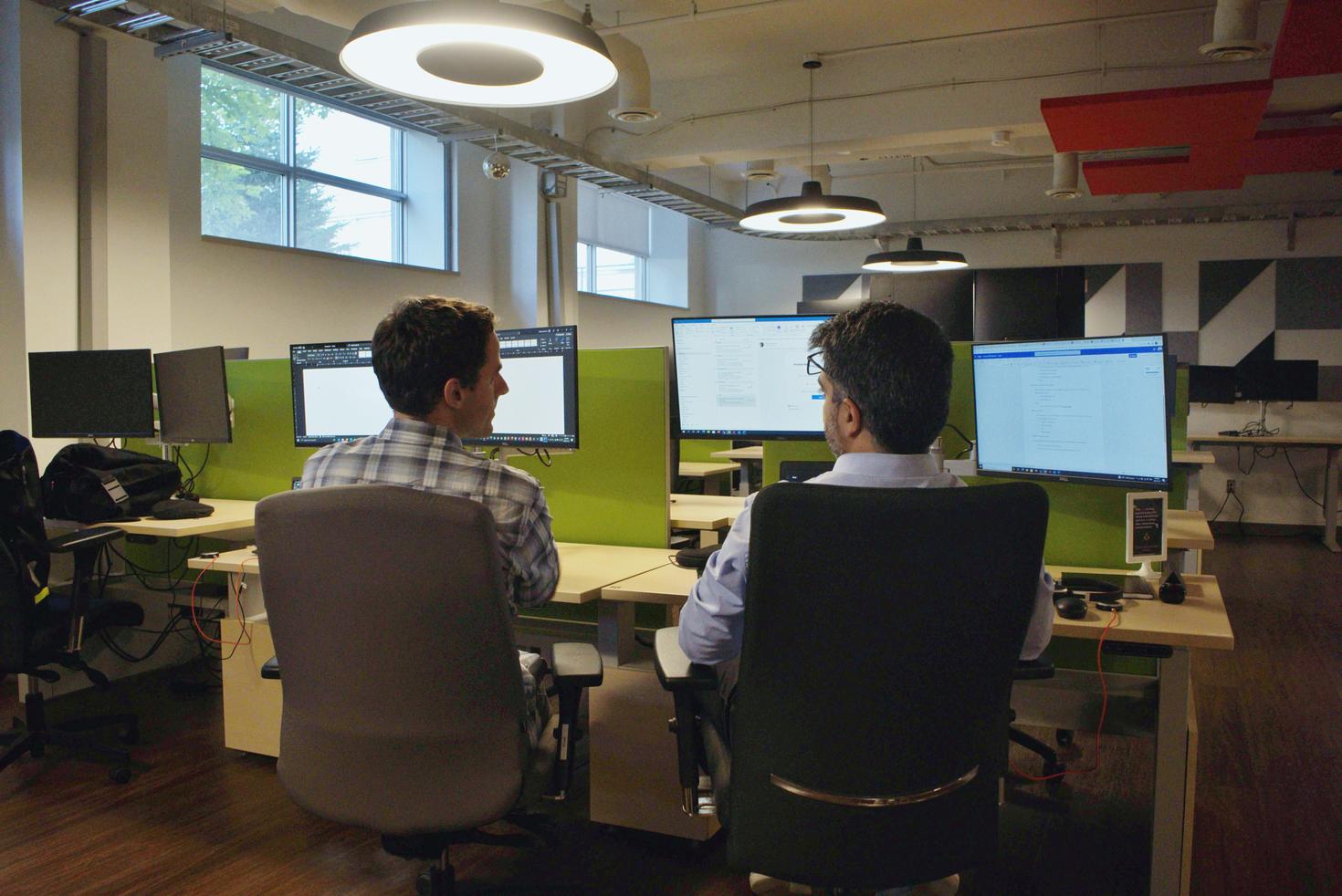 Two men talking at shared work space. 