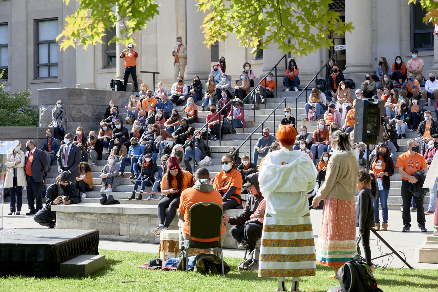 Image shows a seated crowd observing a group of drummers in the foreground