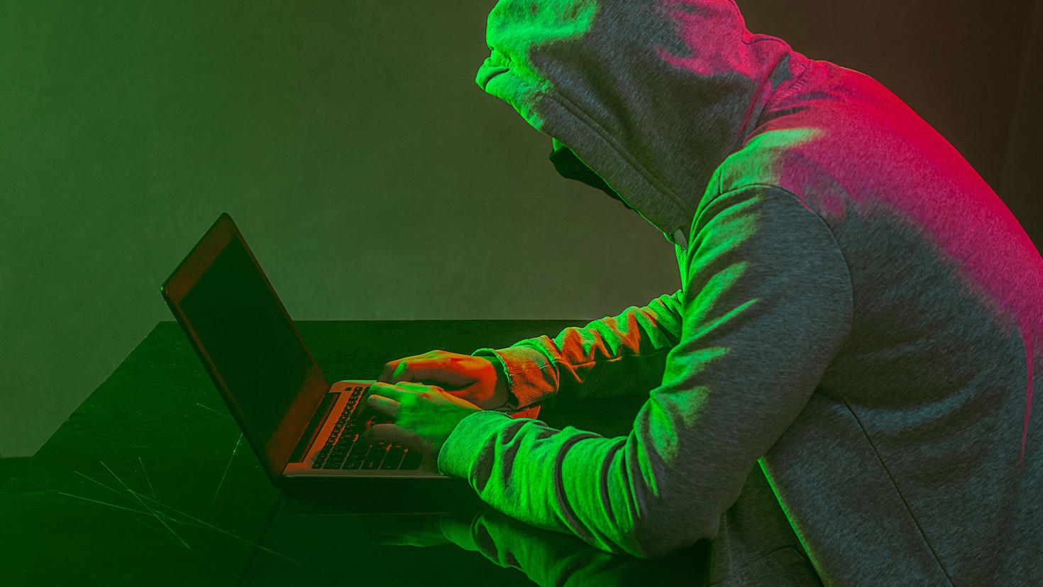 Hooded computer hacker stealing information with laptop.