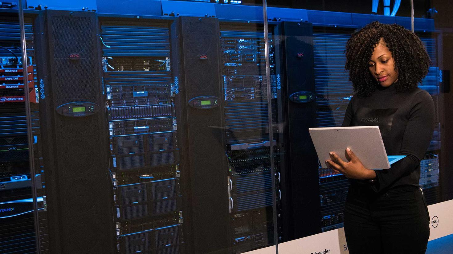 Women with a computer standing in a server room performing maintenance tasks.