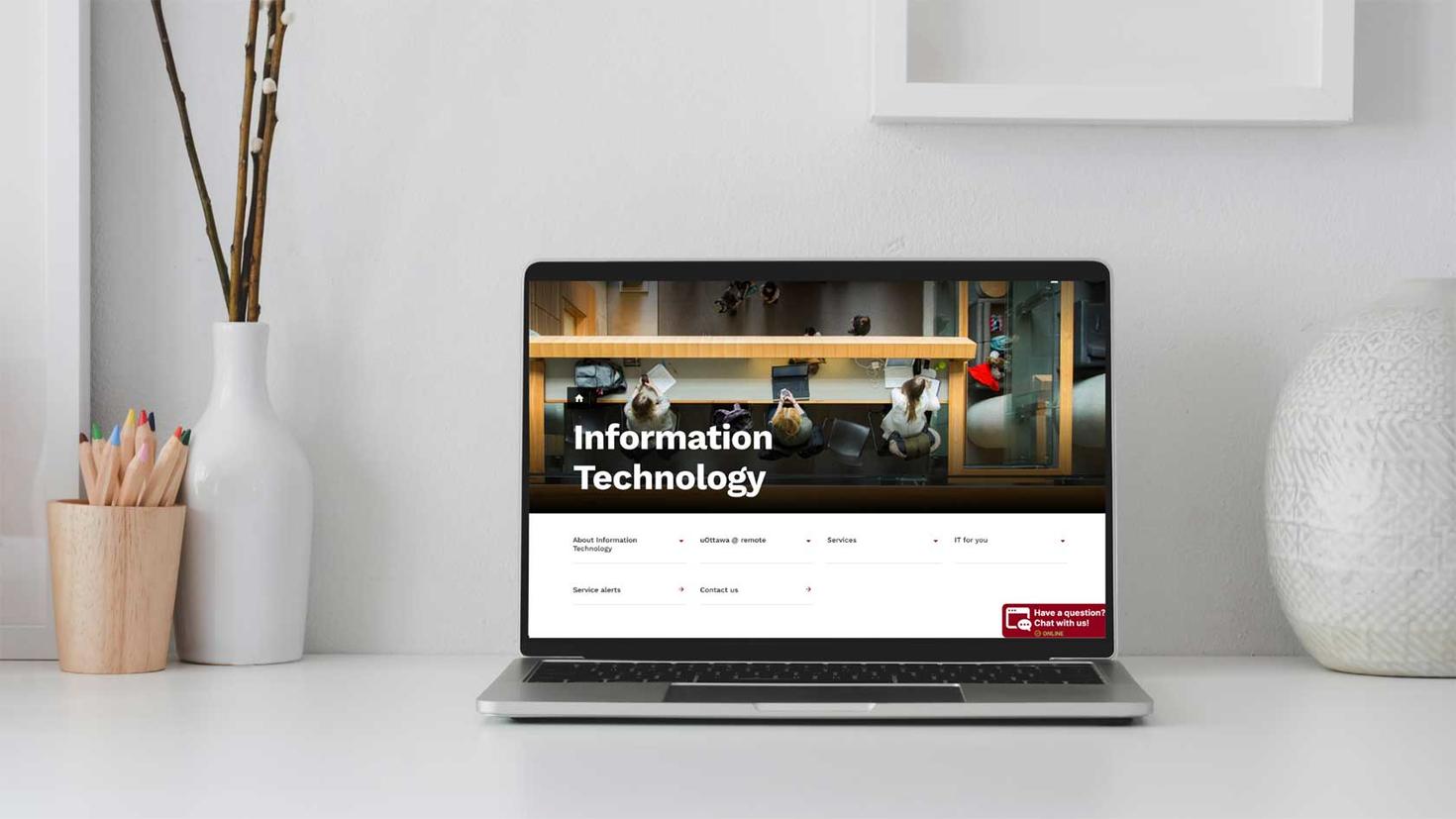 A laptop on a desk displays the new IT website homepage.