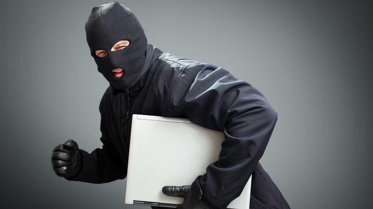 Hooded person stealing a laptop.