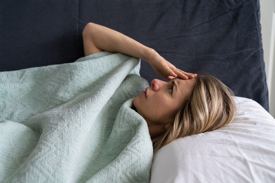 Woman in bed with hand on forehead and headache