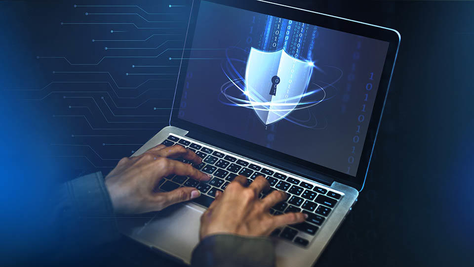 Hands typing on a laptop displaying a shield shaped lock 