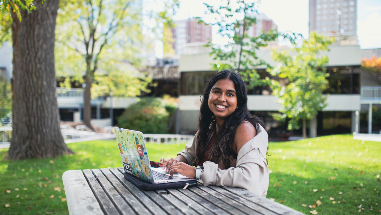 A student working on a laptop on a picnic table outside