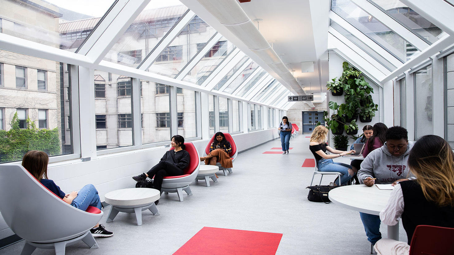 Hallway filled with windows on campus with students working at desks and chairs.