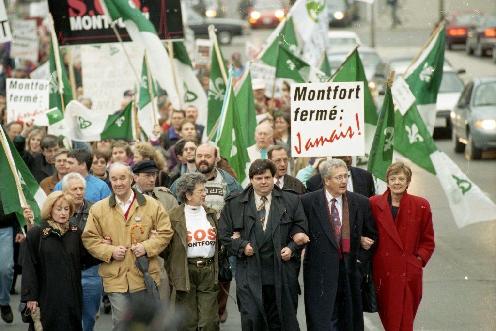Group of people marching and carrying banners and franco-ontarian flags