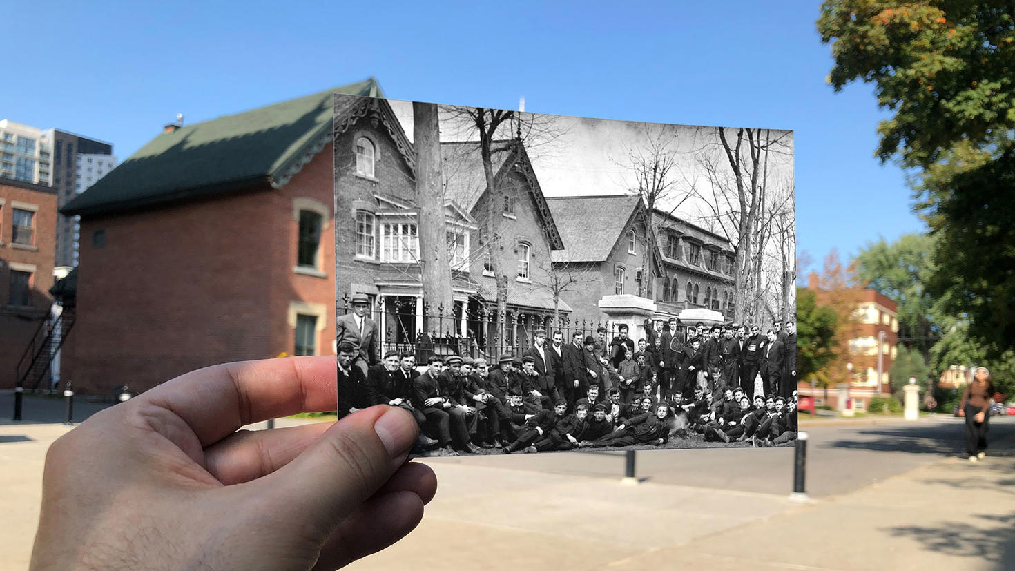 Alumni Hall with a hand holding up an old image of what Alumni Hall looked like in the mid-1800s.