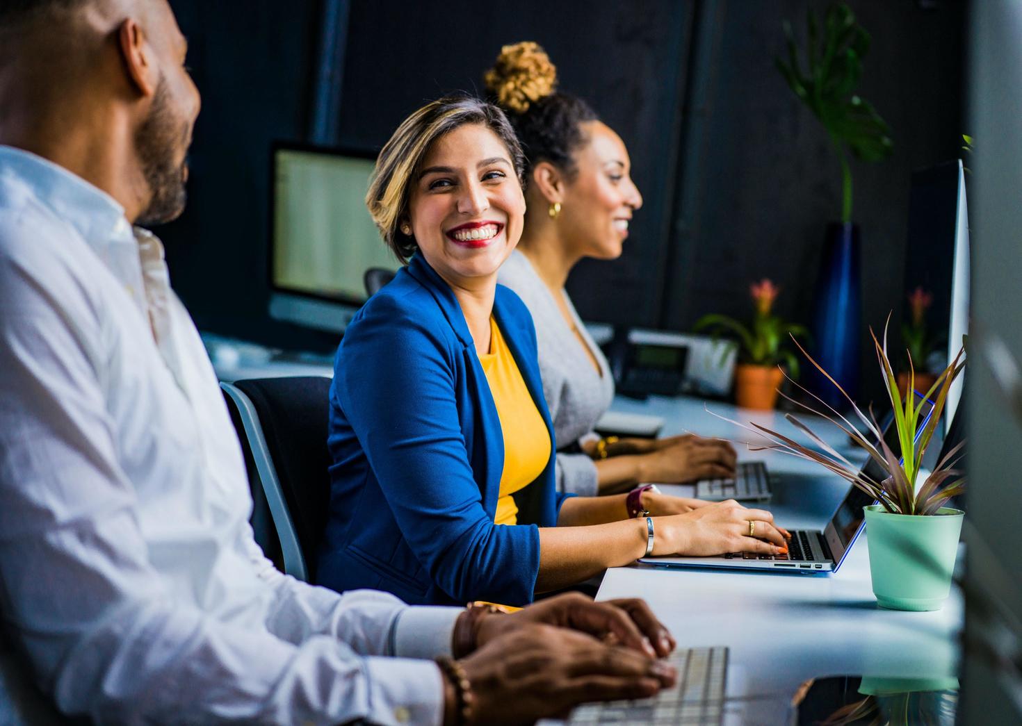 People smiling while working at desks with computers.