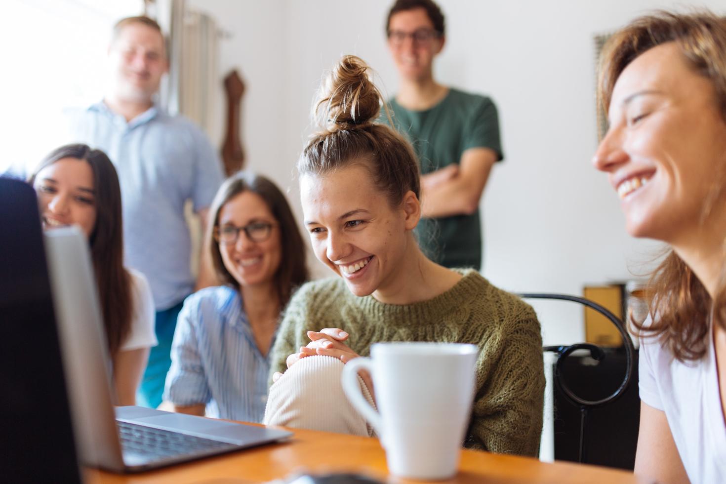 A group of young professionals gathered around a laptop smiling at the screen