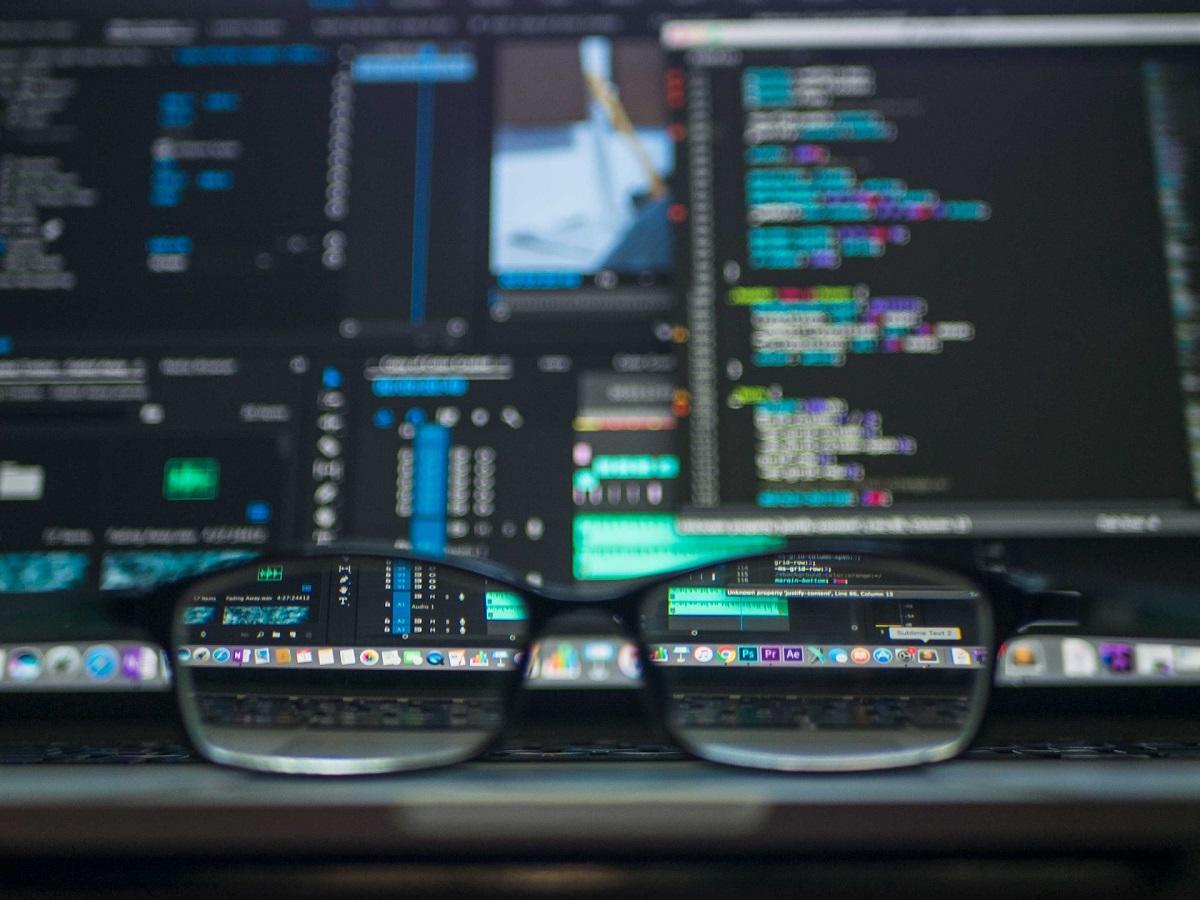 Glasses on desk in front of computer screens