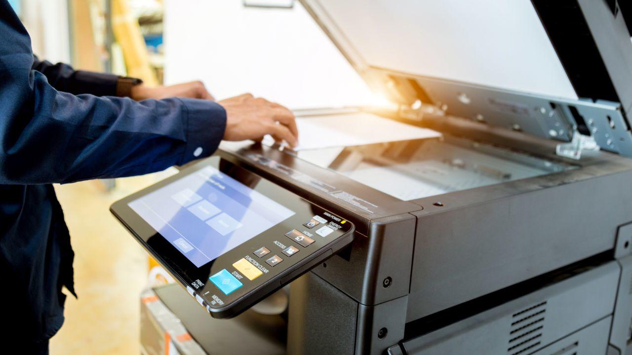 Image showing a man using an office printer by placing a sheet of paper to be copied inside a building 