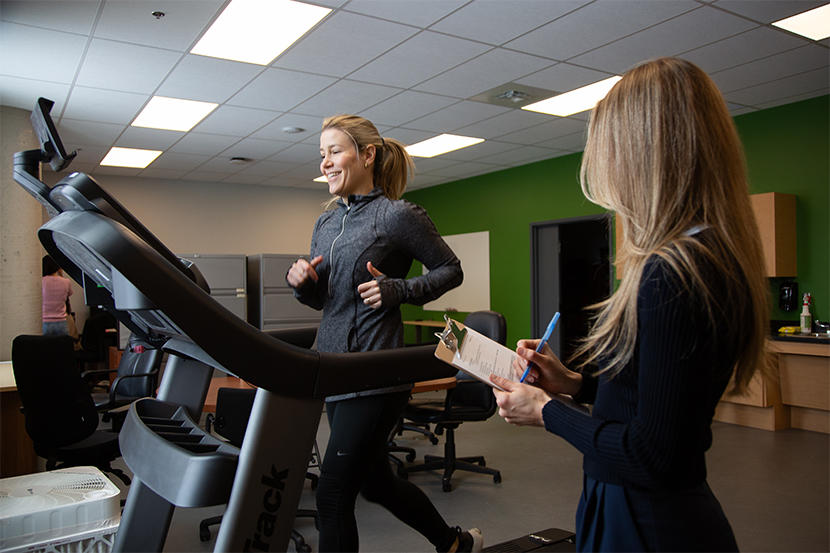 Research scientist Flavia Ignacio Antonio running on a treadmill and research associate Grace Collins taking notes on a clipboard