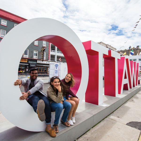 Three students sitting in the O of a large Ottawa sign