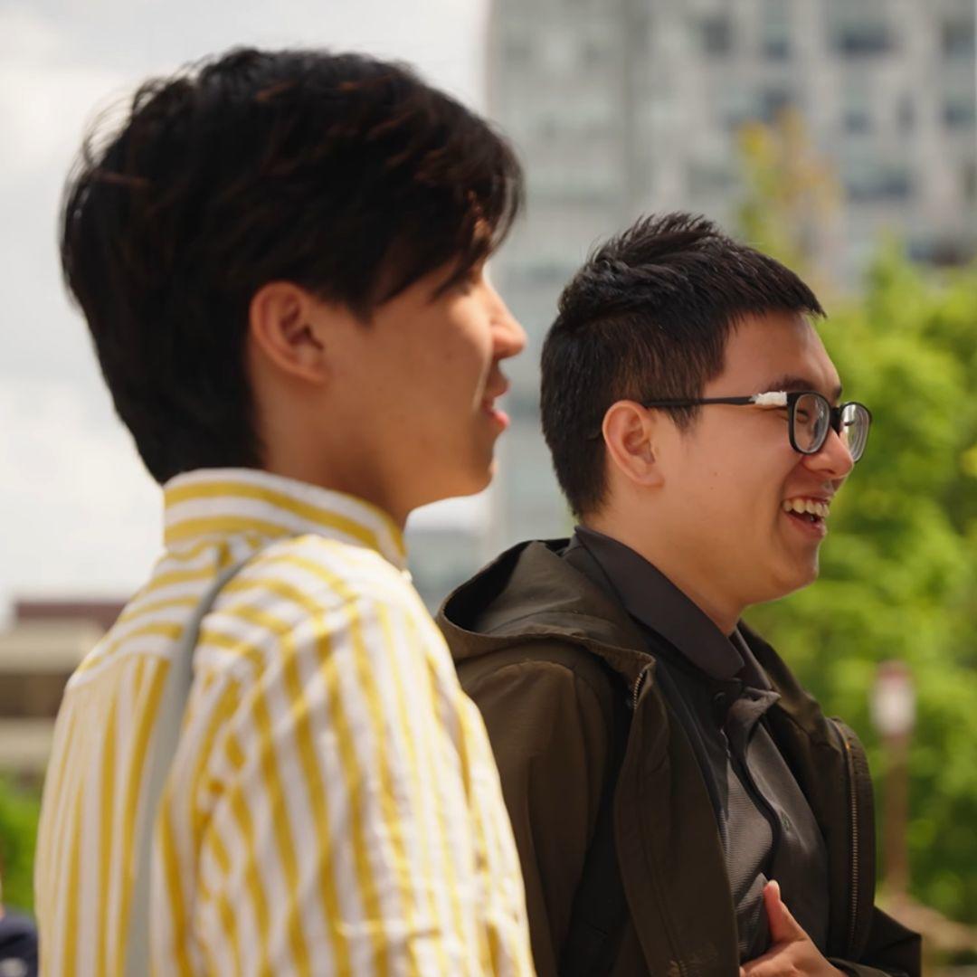 Two students standing next to each other. One of them is laughing.