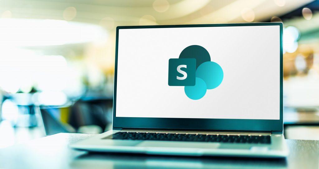 Laptop on desk displaying a white screen with the Microsoft SharePoint logo 
