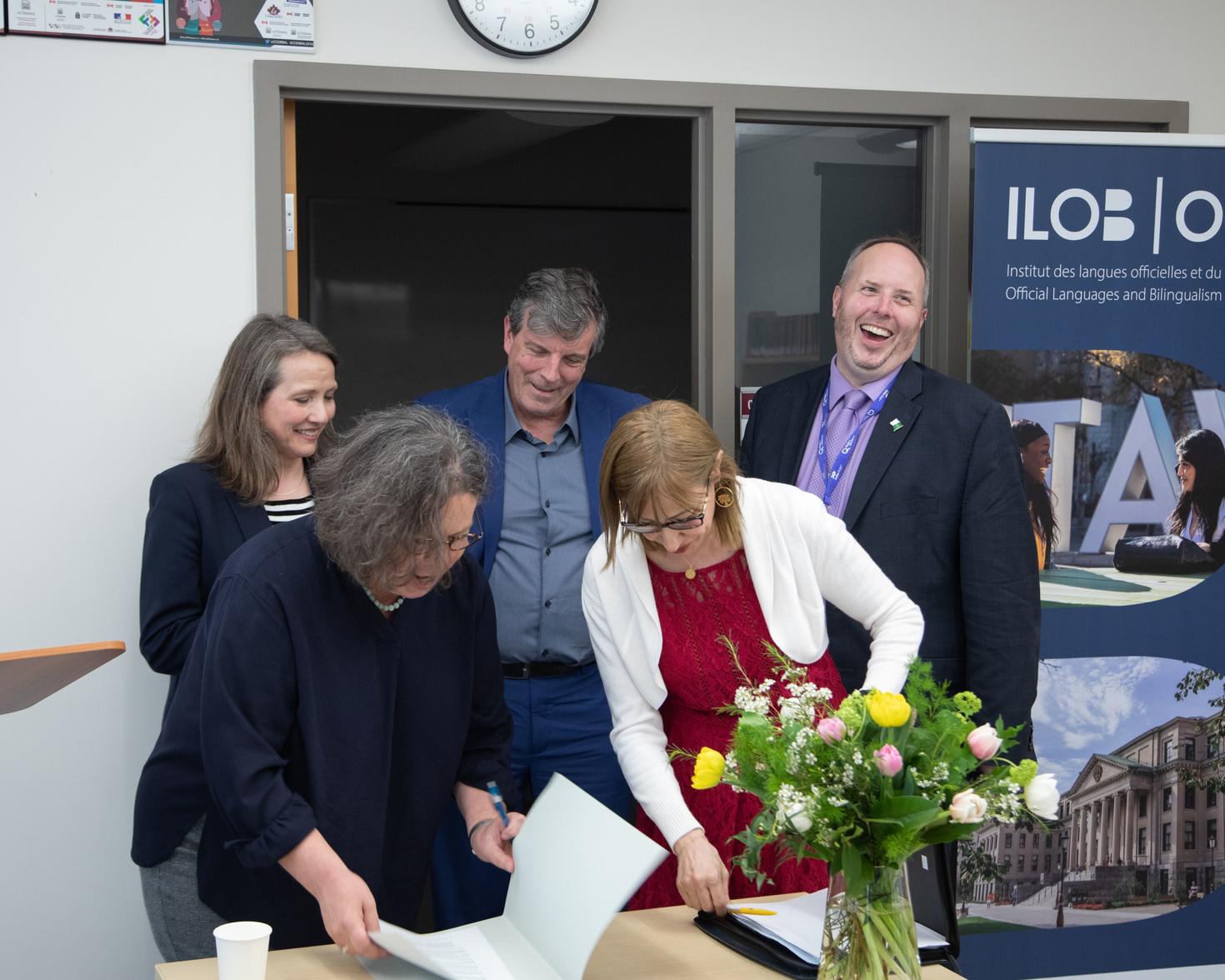 Catherine Buchanan signing a document surrounded by 4 other people.
