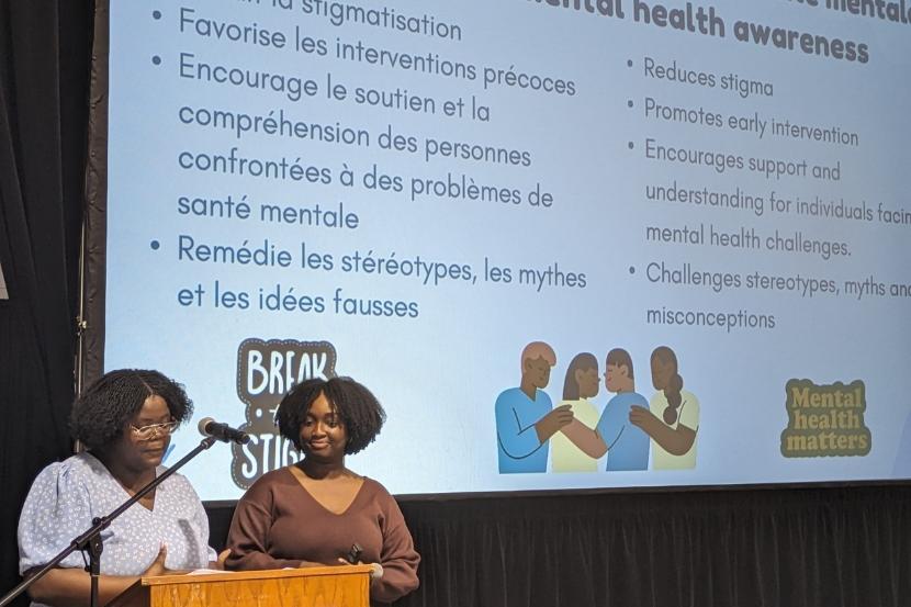 Wina Darius and Grace Jacob, doctoral candidates in clinical psychology, in front of a screen, presenting on how important it is for young people to take care of their mental health by discussing the myths and realities of mental health and the impact of raising awareness.