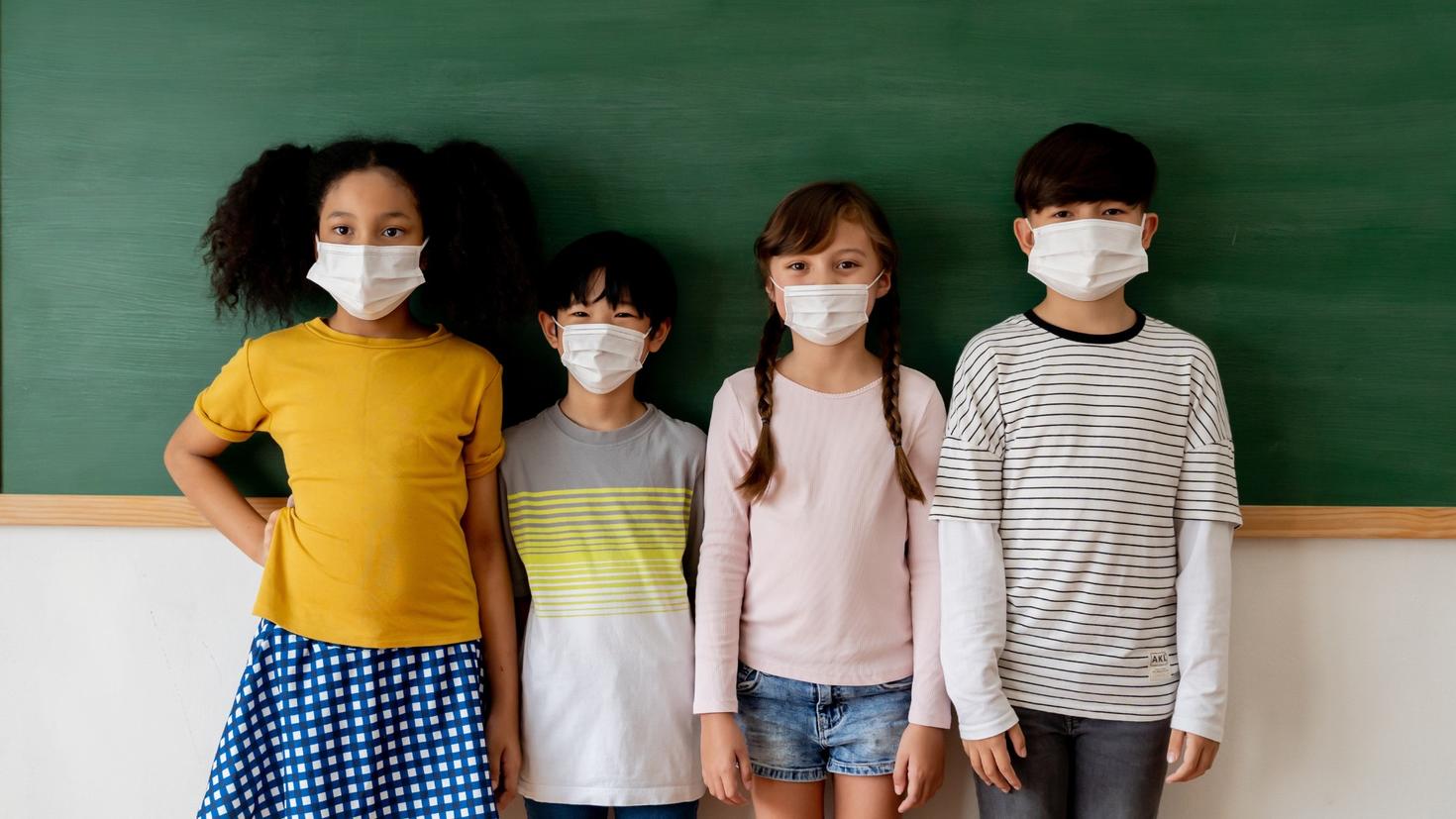 Young students wearing masks, standing in front of a chalkboard