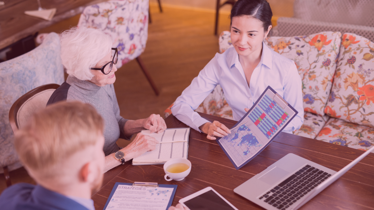 Three people sitting at a table with documents, a laptop, and a cup of tea.