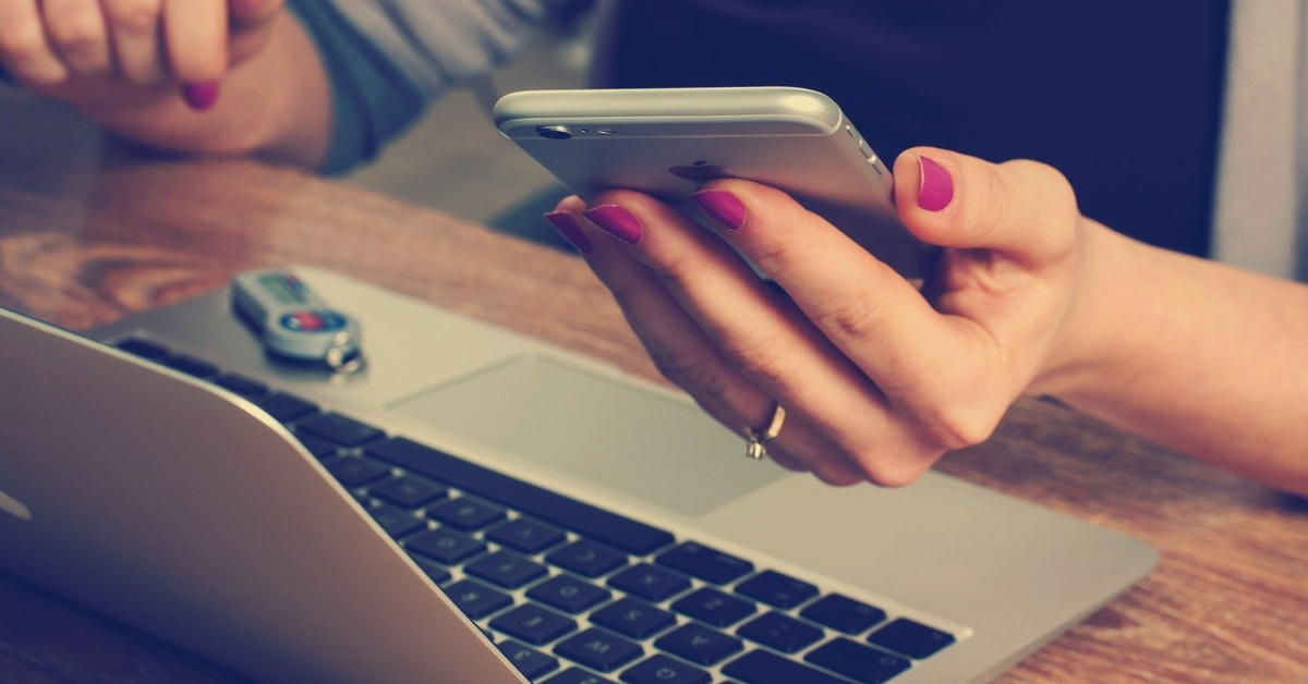 A woman using a smartphone and a laptop computer.