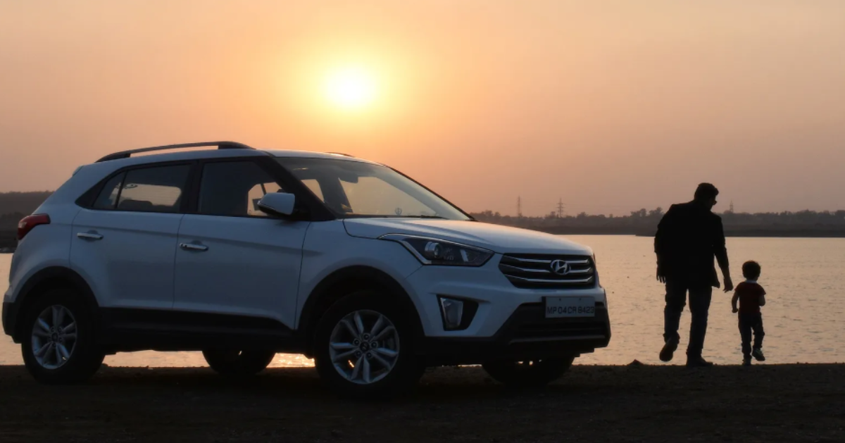 An adult with a child, next to a car