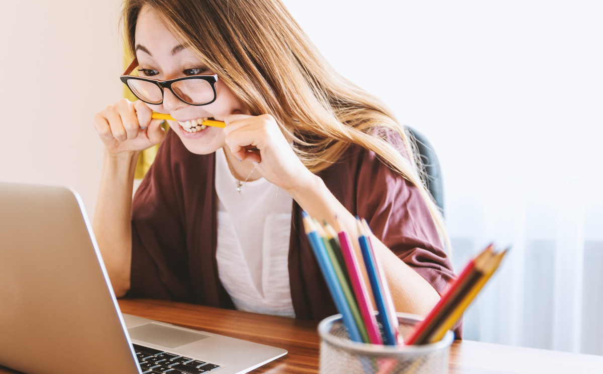 A woman facing a computer and biting a pencil