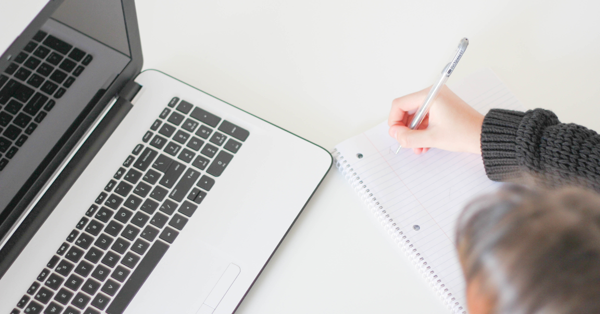 A person working on the computer and taking notes on a pad