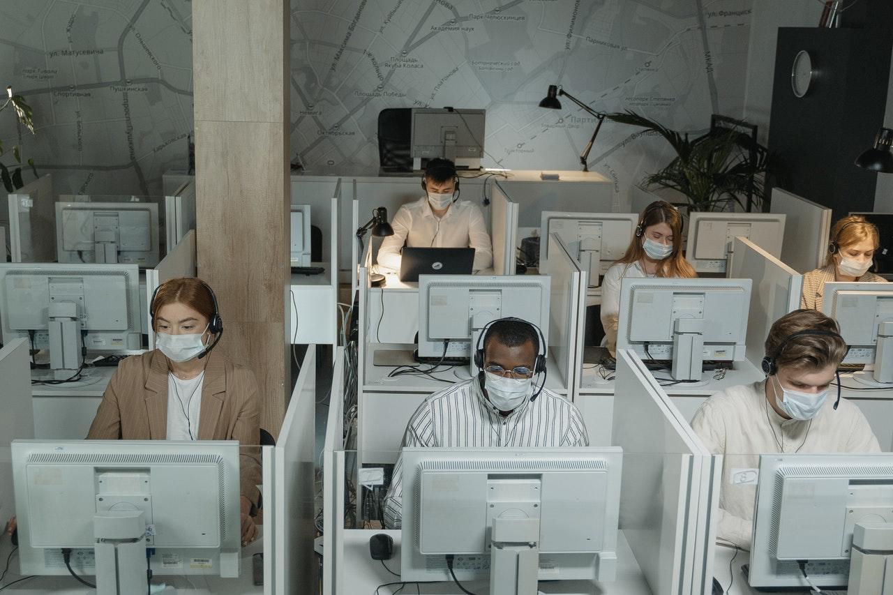 Workers wearing masks sit in crowded cubicles